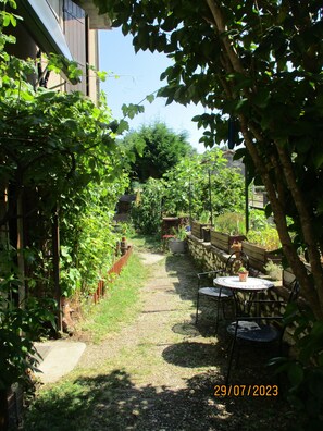 Ein Gartenweg führt zu einer Sitzgelegenheit mit Tisch und Stühlen, umgeben von üppigem Grün und einer Steinmauer.