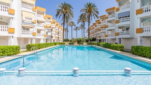 Una piscina con acqua cristallina e azzurra, circondata da edifici bianchi con balconi e palme sullo sfondo.