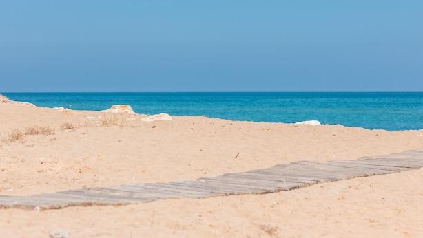 Una spiaggia sabbiosa con una passerella in legno che conduce all'acqua.