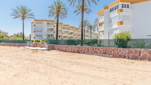 Un hotel sulla spiaggia con diversi balconi, palme e una zona di spiaggia sabbiosa.