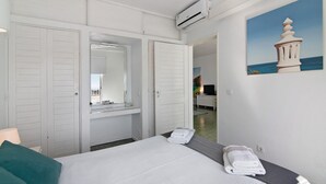 Una camera d'albergo con un letto, uno specchio in bagno, un quadro raffigurante un faro e una porta che dà su un'altra stanza.