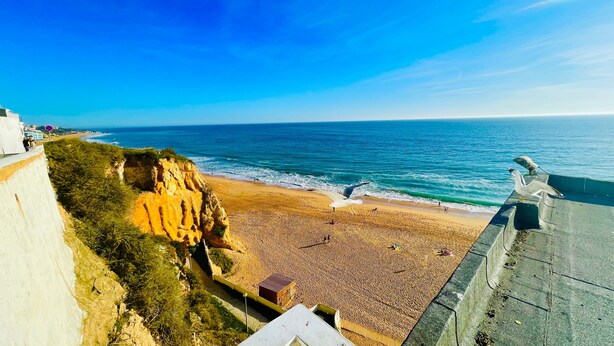 Una spiaggia costiera con cielo sereno, spiaggia sabbiosa e scogliera rocciosa.