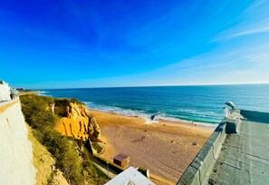 Ein Küstenstrand mit blauem Himmel, sandigem Ufer und einer steilen Felsklippe.