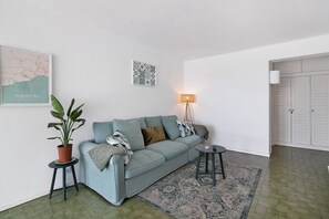 A living room with a sofa, a small table, a lamp, a potted plant, and a map on the wall.