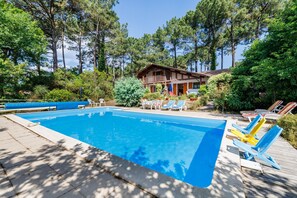 Une piscine entourée d’arbres et d’une construction en bois, avec des chaises longues à proximité.