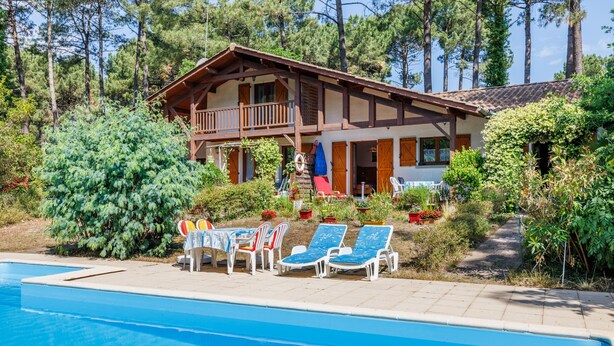 Un chalet à deux étages doté d’un balcon, d’une piscine et de chaises longues.