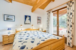 Une chambre à coucher avec un lit en bois, une table de chevet, une lampe, une fenêtre avec des rideaux et des tableaux accrochés au mur.