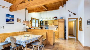Une table à manger en bois avec des bancs, un coin cuisine avec des meubles en bois, et une vue sur la mer par une fenêtre.