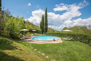 A swimming pool with lounge chairs and umbrellas, surrounded by greenery and trees. - Antique Barn Studio with Pool (Radicondoli (Siena))