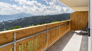A balcony with a wooden railing, a chair, and a view of a forested mountain range. - Apartment 'Haughof - Blumenwiese' with Mountain View, Wi-Fi & Balcony, Very Quiet Location (Vöran bei Meran)