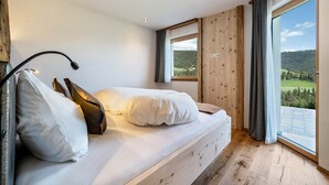 A bedroom with a bed, a window with curtains, and a view of a forested area. - Apartment 'Haughof - Blumenwiese' with Mountain View, Wi-Fi & Balcony, Very Quiet Location (Vöran bei Meran)