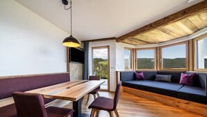 A modern interior with a wooden dining table, cushioned seating, and large windows offering a view of the outdoors. - Apartment 'Haughof - Blumenwiese' with Mountain View, Wi-Fi & Balcony, Very Quiet Location (Vöran bei Meran)