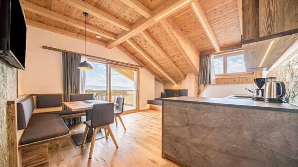 Una cocina moderna con encimera de mármol, vigas de madera en el techo y un comedor con banco y sillas.