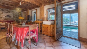 A dining area with a table set for two, wooden chairs, a wooden cabinet, and a view through a door to an outdoor deck. - 'Ferme de Faustine' Apartment with Shared Heated Pool and Wi-Fi (Saint-Gervais-les-Bains)