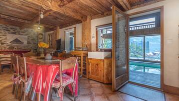 Un coin repas avec une table dressée pour deux personnes, des chaises en bois, un buffet en bois et, vue à travers une porte, une terrasse extérieure.