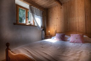 Une chambre à coucher aux murs lambrissés, avec un lit, une fenêtre avec des rideaux et une table de chevet surmontée d’une lampe.