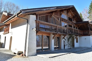 Un chalet en bois à deux étages, doté d’un balcon, d’une base en pierre et d’une allée gravillonnée.
