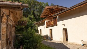 A rustic building with a wooden balcony, a stone wall, and a gravel path. - 'Ferme de Faustine' Apartment with Shared Heated Pool and Wi-Fi (Saint-Gervais-les-Bains)