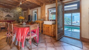 A rustic dining area with a wooden ceiling, stone wall, and a view through a glass door.