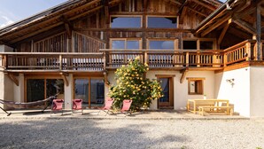 A wooden chalet with a balcony, a dining area, and a large window.