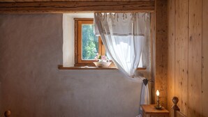 A bedroom with a wooden ceiling, a window with a view of greenery, a bedside table with a candle, and a bed with a checkered blanket.