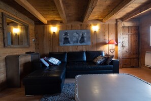 A wooden cabin interior with a black leather sofa, a white table, and a painting of bears on the wall.