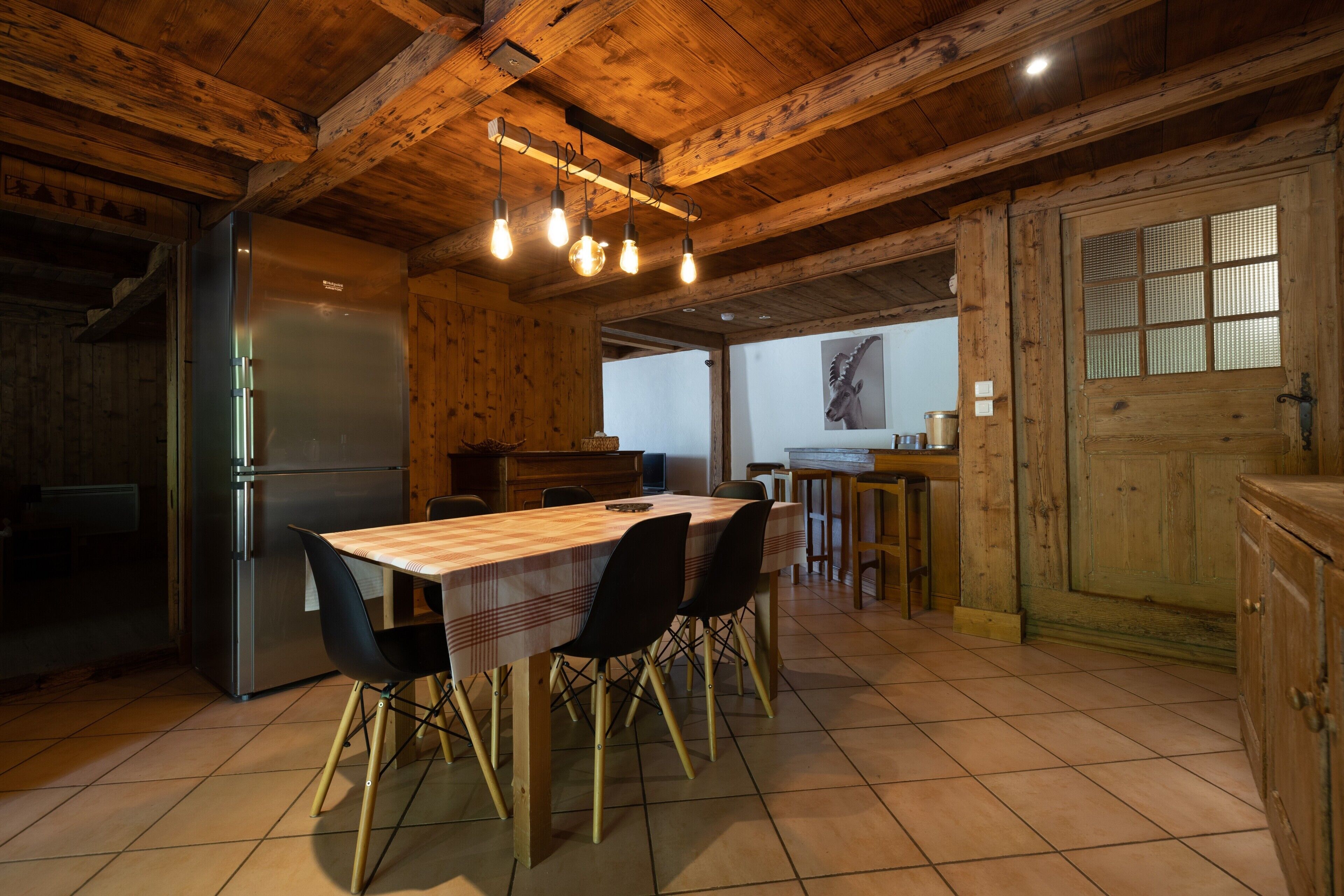 A wooden interior with a dining table, chairs, a refrigerator, and a window.