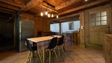 A wooden interior with a dining table, chairs, a refrigerator, and a window.