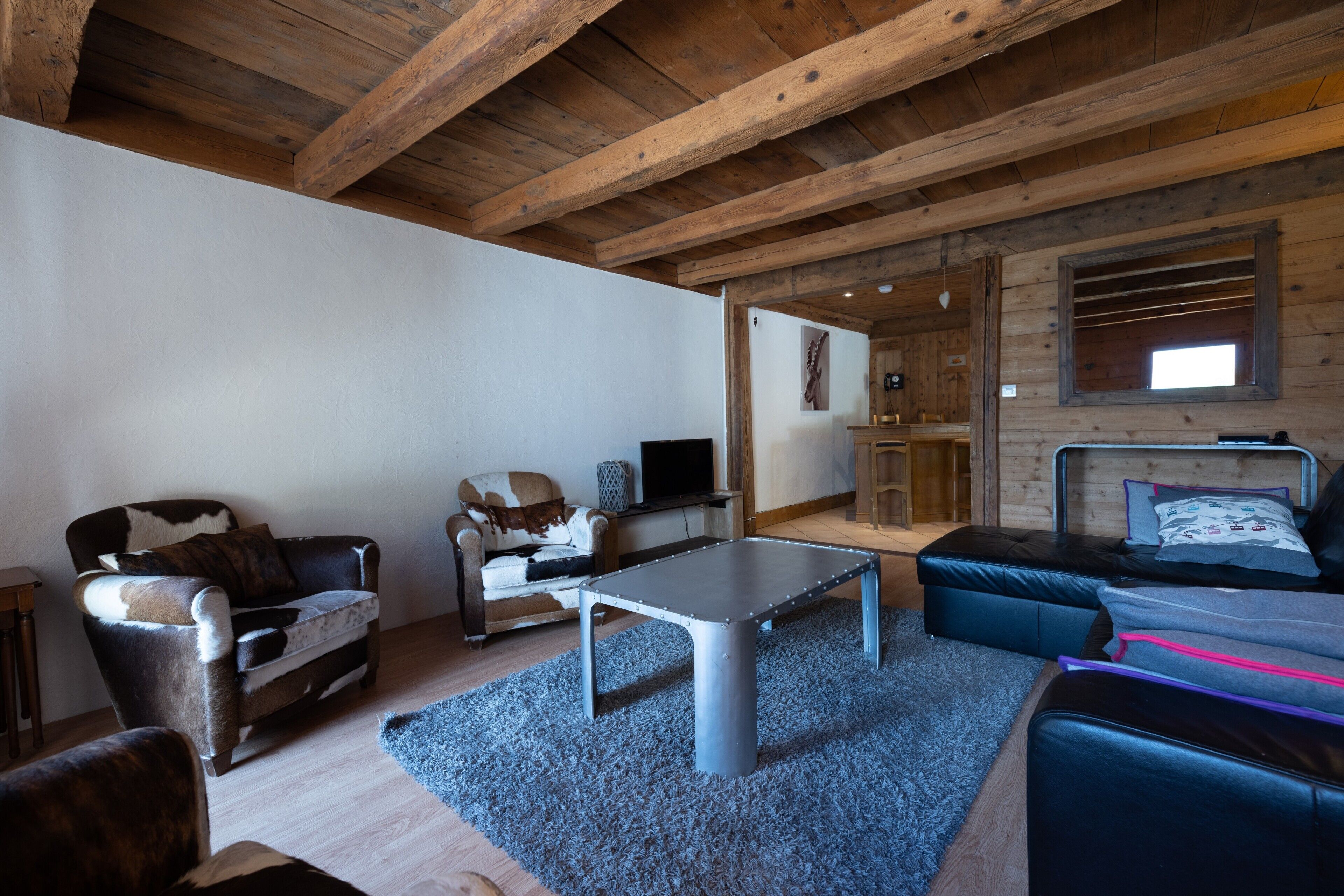 A rustic cabin interior with a wooden ceiling, a sofa, a table, and a bed.