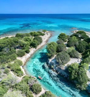 Luftaufnahme einer Küstenlandschaft mit klarem türkisblauem Wasser, dichtem Grün und felsigem Gelände.
