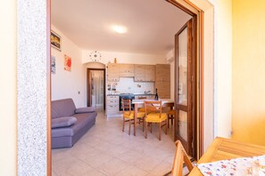 Un espace de vie compact comprenant un coin cuisine, un coin repas avec des chaises, un canapé et une petite table.