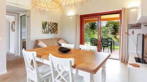A dining area with a wooden table, white chairs, a woven light fixture, and a view of the outdoors through a glass door. - La casa di Debora with A/C & Wi-Fi – Modern Apartment near La Cinta Beach (San teodoro)