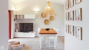 A dining area with a wooden table and white chairs, a television, and wall-mounted artwork. - La casa di Debora with A/C & Wi-Fi – Modern Apartment near La Cinta Beach (San teodoro)