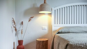 A bedroom with a white headboard, a bedside lamp, a wooden stool, and a vase with dried plants. - La casa di Debora with A/C & Wi-Fi – Modern Apartment near La Cinta Beach (San teodoro)