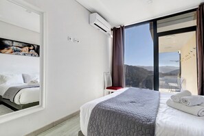 Hotellihuone, jossa on suuri sänky, tuoli, seinällä taulu ja näkymä ulos.