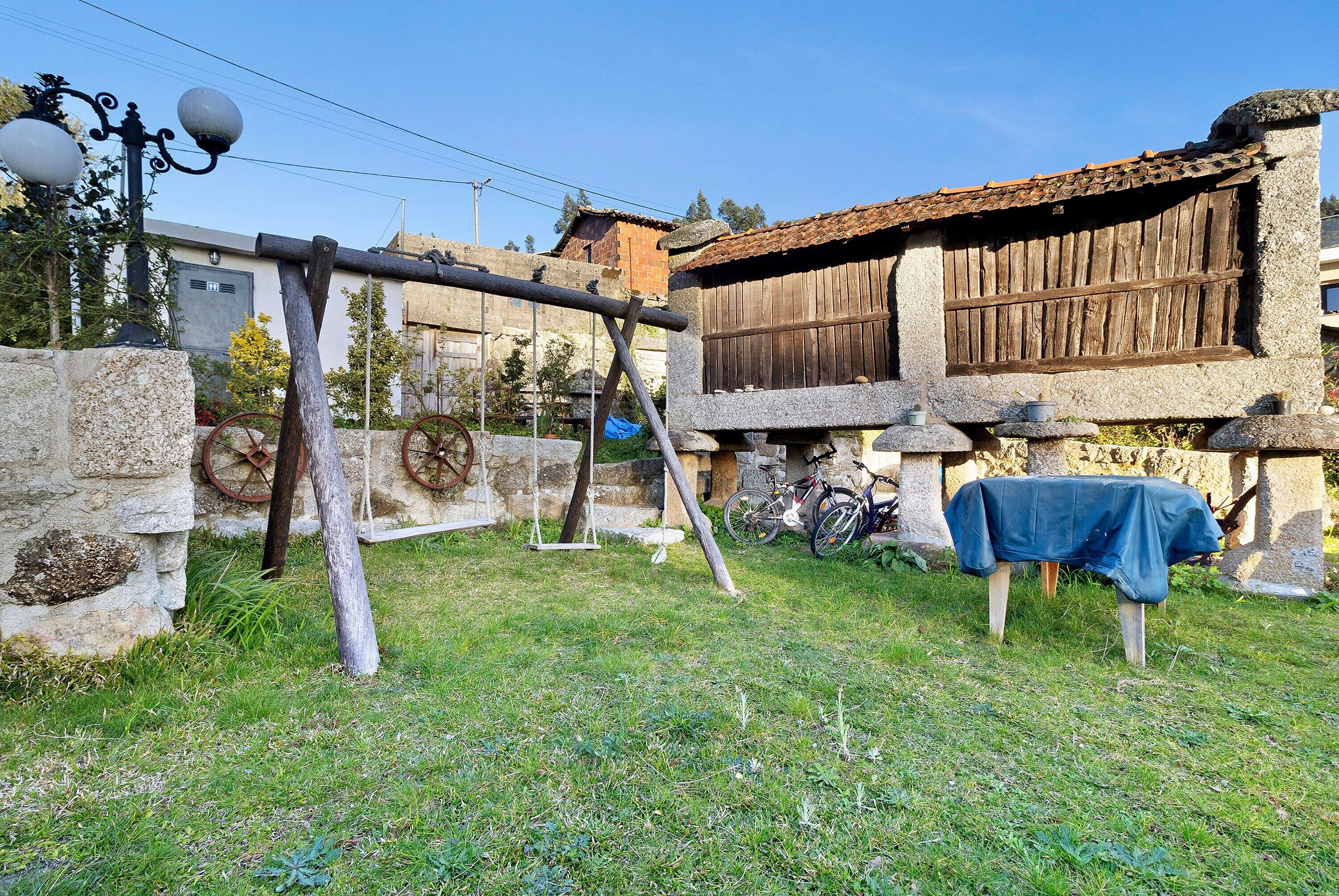 A rustic outdoor area with stone walls, a wooden structure, and a table covered with a blue cloth.