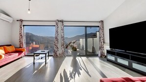 A modern living room with a sofa, a coffee table, a TV, and a large window with curtains.
