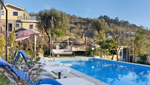 A swimming pool with lounge chairs, a covered seating area, and a view of a hillside.