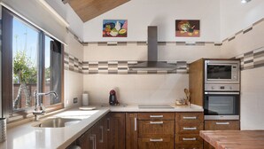 Una cocina con un lavamanos de acero inoxidable, armarios de madera, horno empotrado y una ventana con vistas al exterior.