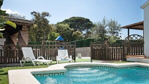 Un patio trasero con piscina, valla de madera y un porche cubierto.