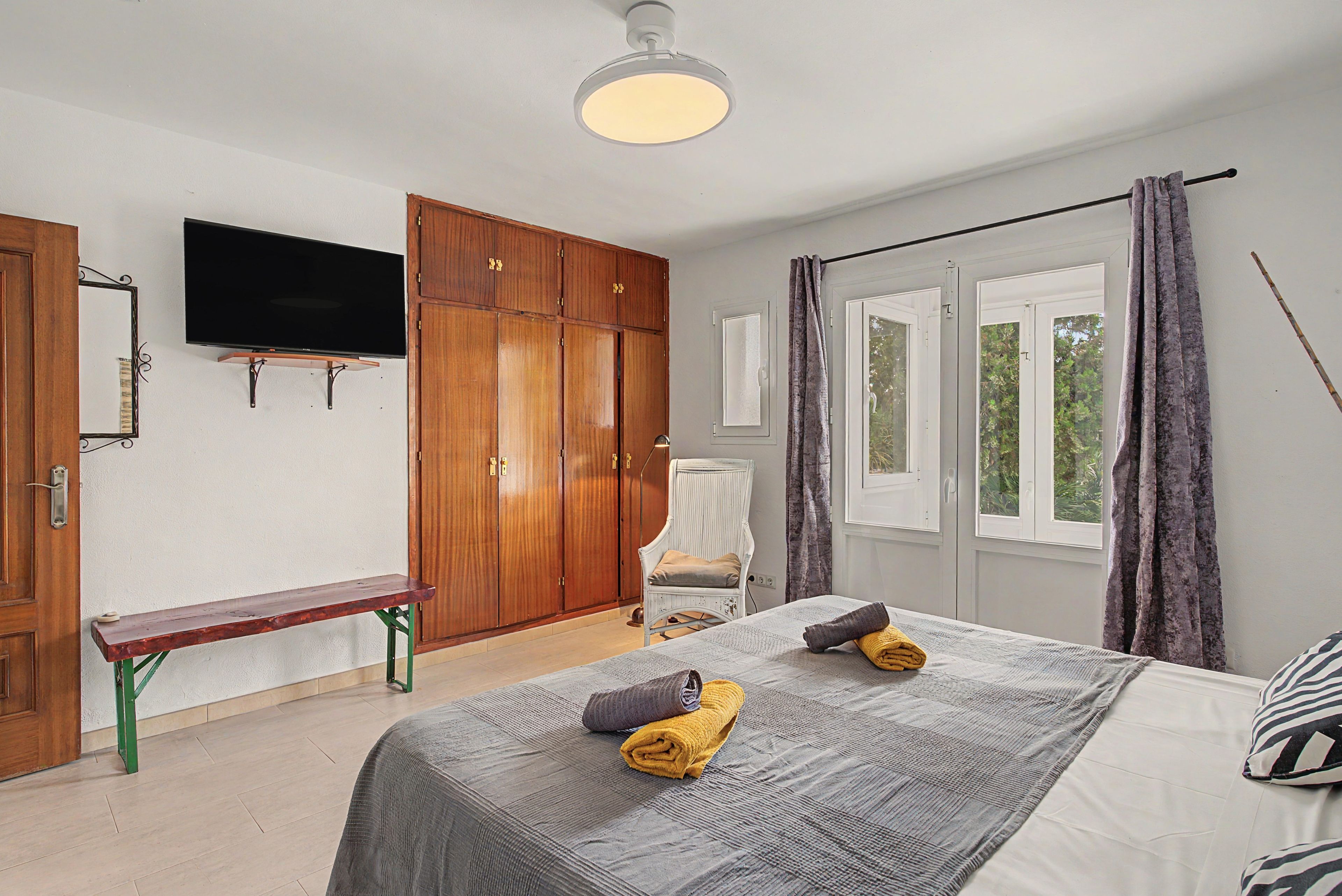 Een slaapkamer met een bed, een bankje, een televisie en een kledingkast.