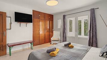 Een slaapkamer met een bed, een bankje, een televisie en een kledingkast.