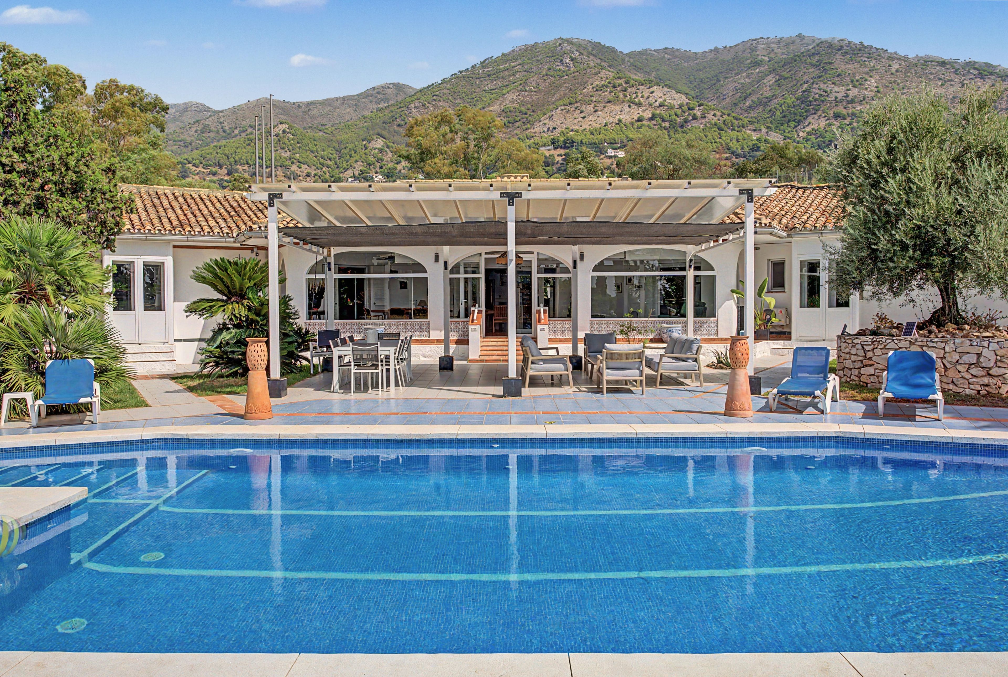 A pool area with a covered patio, seating, and a view of mountains.