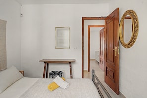 Un dormitorio con cama, una mesita, un espejo y una puerta que da a otra habitación.