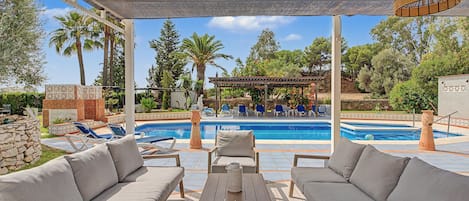 A covered outdoor area with a pool, lounge chairs, and a pergola.