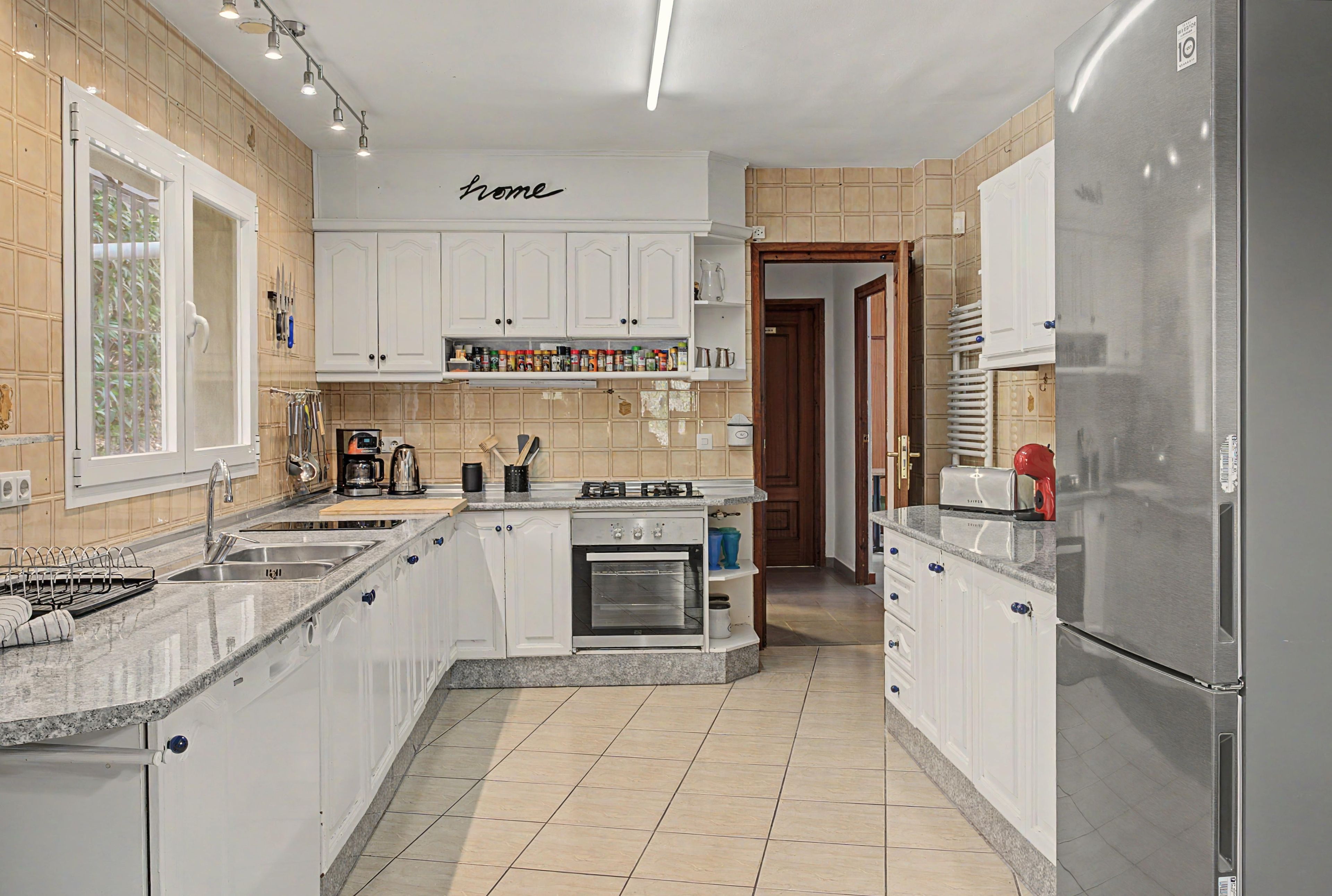 A modern kitchen with white cabinetry, a built-in oven, and a stainless steel refrigerator.