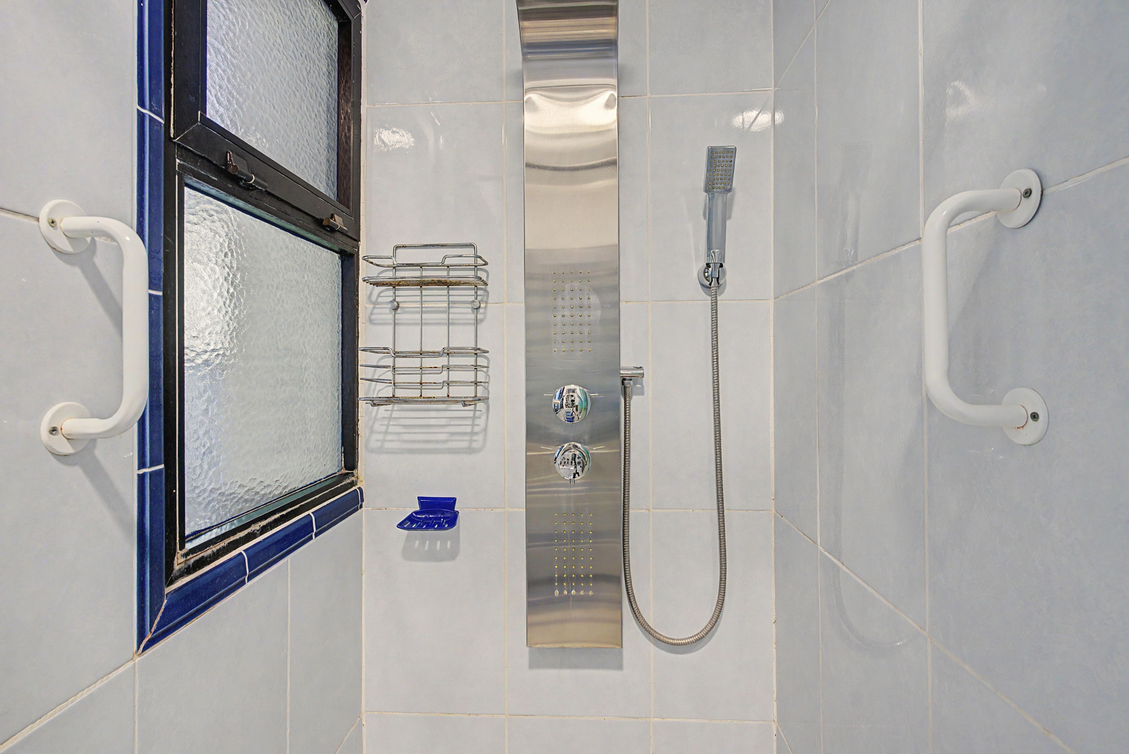 A bathroom with a shower, a towel rack, and a window with a blue frame.