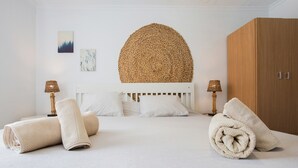 A neatly made bed with rolled towels, a round woven headboard, and a wooden wardrobe. - Apartment 'El Cotillo Mar Beach' with Sea View, Terrace & Wi-Fi (El Cotillo)