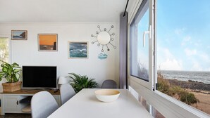 A room with a dining table, chairs, a TV, a bowl, and a view of the beach. - Apartment 'El Cotillo Mar Beach' with Sea View, Terrace & Wi-Fi (El Cotillo)