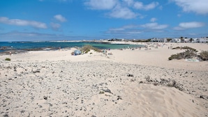 A beach with rocky terrain, a few people, and buildings in the background. - Apartment 'El Cotillo Mar Beach' with Sea View, Terrace & Wi-Fi (El Cotillo)